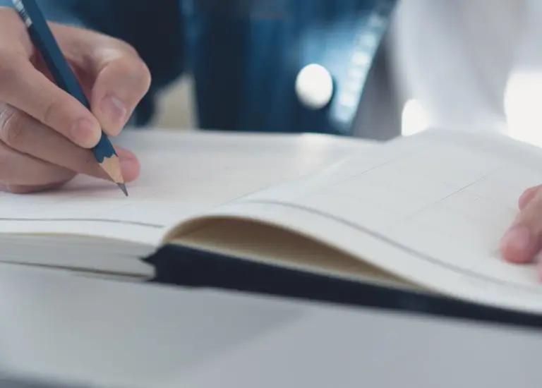 a person writing on a notebook with a pen